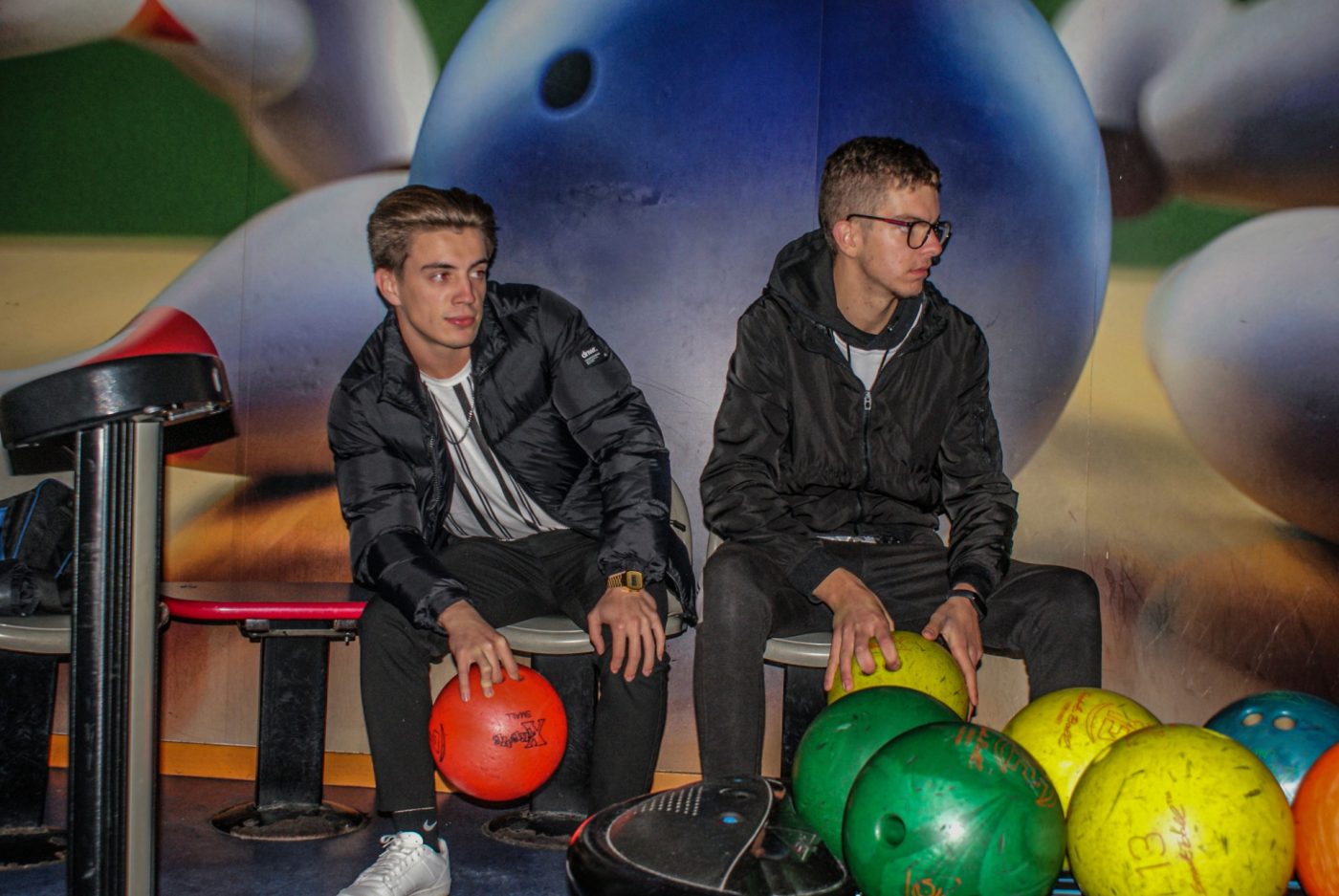 Dois jovens sentados junto às bolas de bowling coloridas no Good Bowling