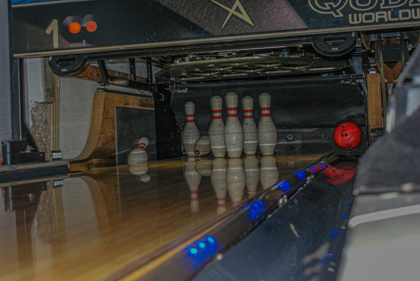 Pinos ao fundo de uma pista de bowling com bola vermelha
